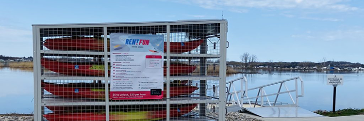 Kayaks locked up by the lake with a sign that labels "Rent.Fun" on it.