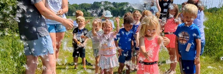 Many children laughing and smiling in the sun playing with large dandelions in the wind. 