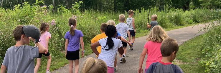 Multiple children walking ahead on a sunny trail in a park.