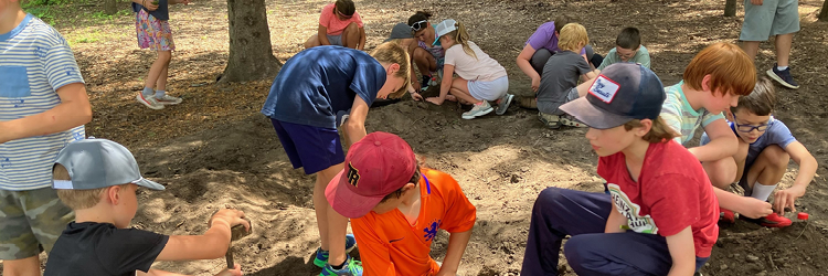 Many children playing in the dirt with sticks and rocks. 