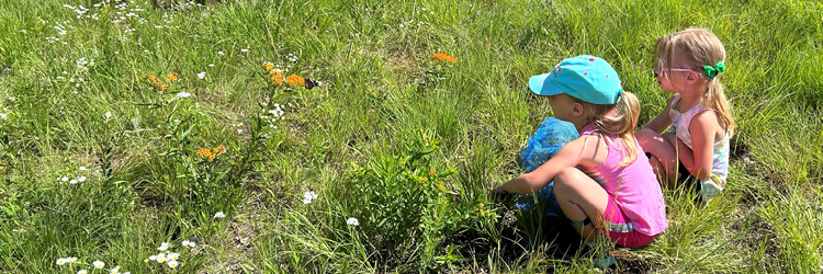 Two girls dressed in pink sitting in the grass watching monarch butterflies fly.