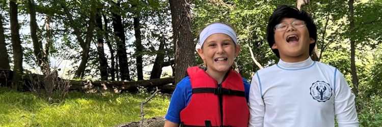 Two boys smiling goofy at the camera with the lake and forest behind them,