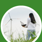 A person with a laptop in a field looking at a wind turbine.