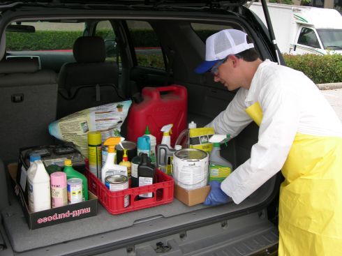 Man in protective garments placing hazardous waste in the trunk of a vehicle.