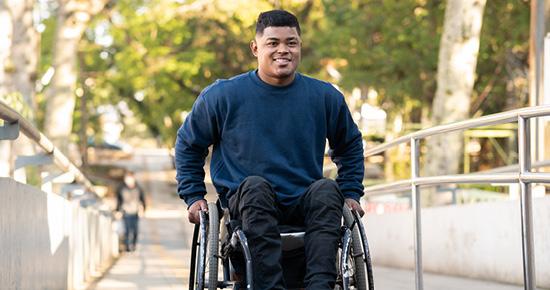 A man in a wheelchair smiles as he reaches the top of an access ramp.